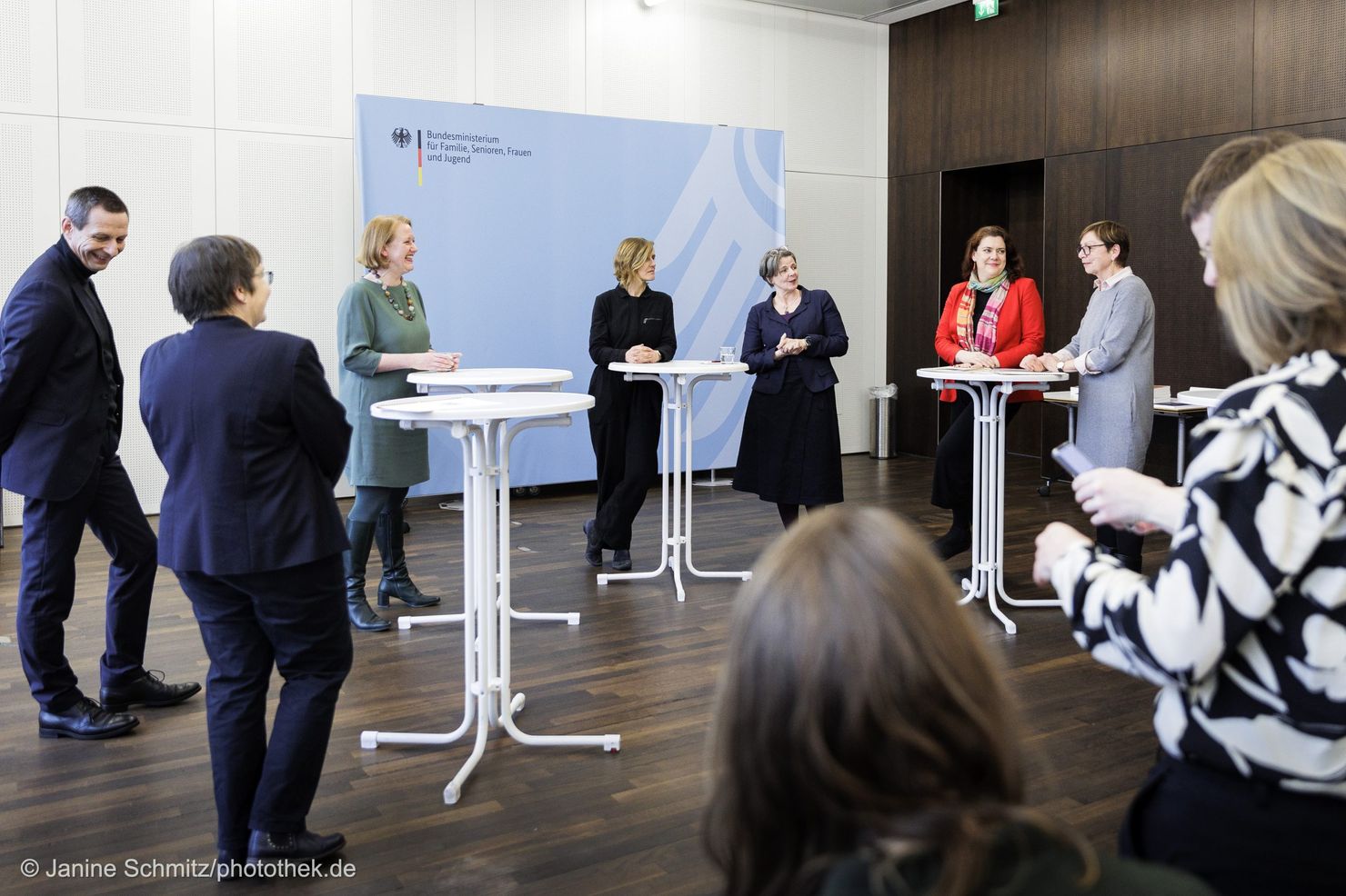 Eine Gruppe von Personen unterhält sich an Stehtischen, vor einem Banner mit der Aufschrift "Bundesministerium für Familie, Senioren, Frauen und Jugend"