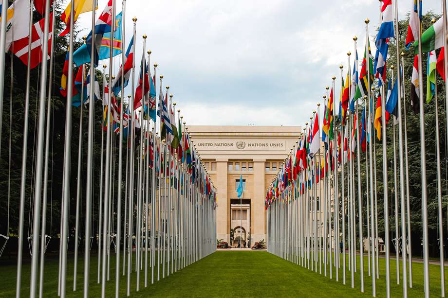 Blick durch zwei Reihen von Länderfahnen auf ein Gebäude mit der Aufschrift "United Nations - Nations Unies".